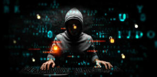 Hooded hacker using two keyboards surrounded by code