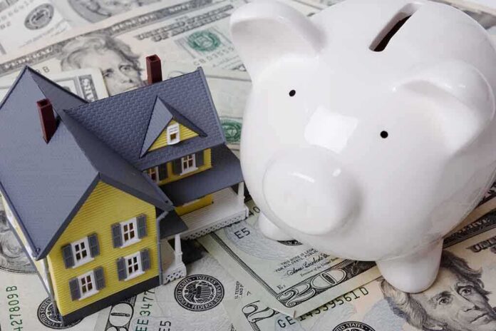 A model house next to a white piggy bank on a bed of dollar bills