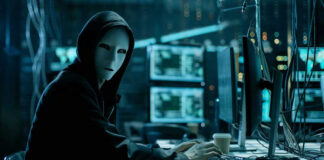 Person wearing mask and hoodie at computer desk