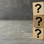 Three wooden blocks with black question marks stacked.