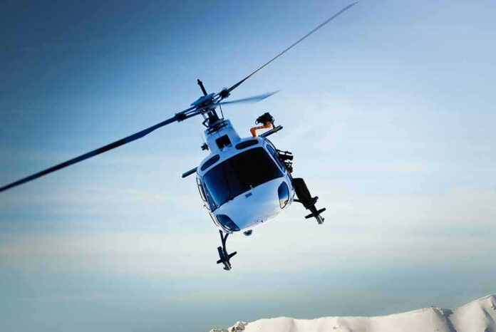 A helicopter flying over a mountainous landscape against a blue sky