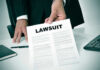 Person holding a document titled LAWSUIT in office.
