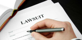 Hand holding pen, filling out lawsuit form.