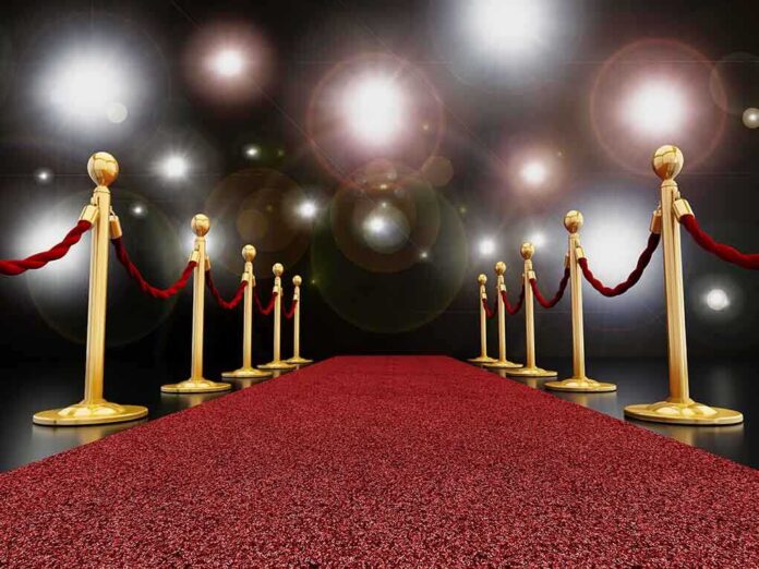 A red carpet lined with gold stanchions and ropes under bright spotlights