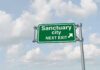 Sanctuary Officials CRIMINALIZED — Prison Time Incoming Green road sign saying sanctuary city next exit
