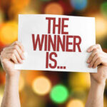 Hands holding a sign reading The Winner Is