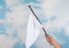 Hand holding white flag against a blue sky.