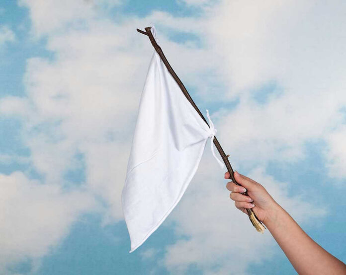Hand holding white flag against a blue sky.