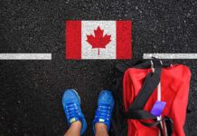 ALARMING Shortcut: Foreign Troops Become Permanent Residents A person's feet next to a red backpack on a road with a Canadian flag painted on it
