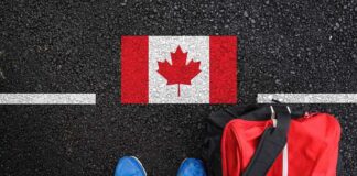 A person's feet next to a red backpack on a road with a Canadian flag painted on it