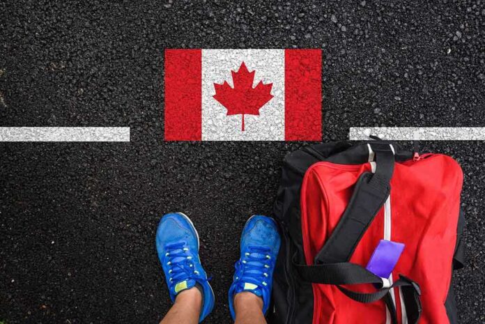 shutterstock_1770402584.jpg A person's feet next to a red backpack on a road with a Canadian flag painted on it