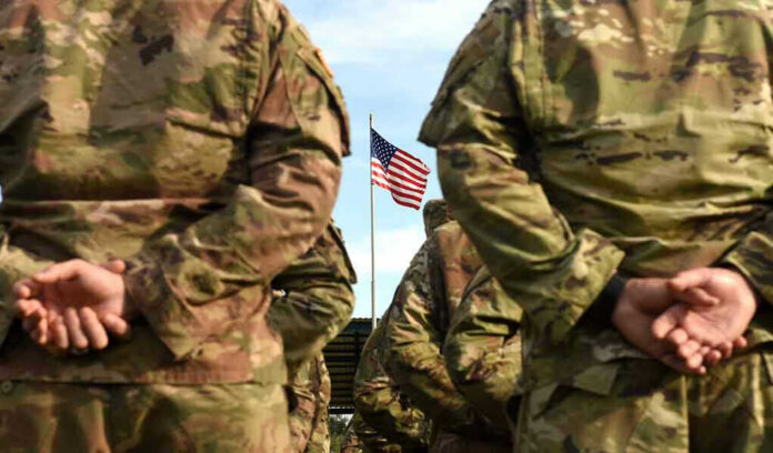 Soldiers stand in formation with American flag in background.