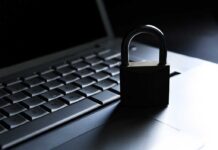 A padlock resting on a laptop keyboard in a dimly lit environment