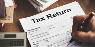 Person filling out a tax return form with a calculator nearby