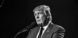 A public figure speaking into a microphone in a serious manner