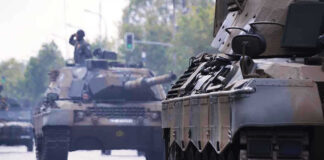 Tanks on a road with soldiers inside.