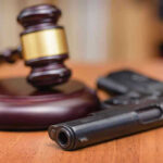 Police SWARM O’Keefe HQ, Guns Taken Gavel and handgun on a wooden surface.