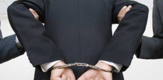 A person in a suit with hands cuffed behind their back