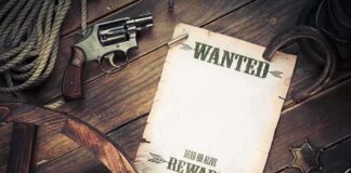 A vintage wanted poster alongside a revolver and rope on a wooden table