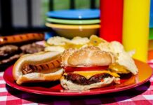 A plate with a hamburger, hot dog, and potato chips on a picnic table