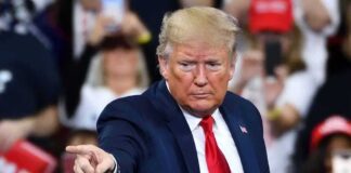 A man in a suit pointing during a speech at a rally