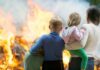 A family watching a large fire outdoors with children in their arms