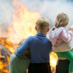 A family watching a large fire outdoors with children in their arms