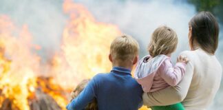 A family watching a large fire outdoors with children in their arms