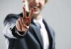 A man in a suit smiling and making a peace sign with his hand