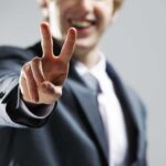 A man in a suit smiling and making a peace sign with his hand