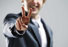 A man in a suit smiling and making a peace sign with his hand
