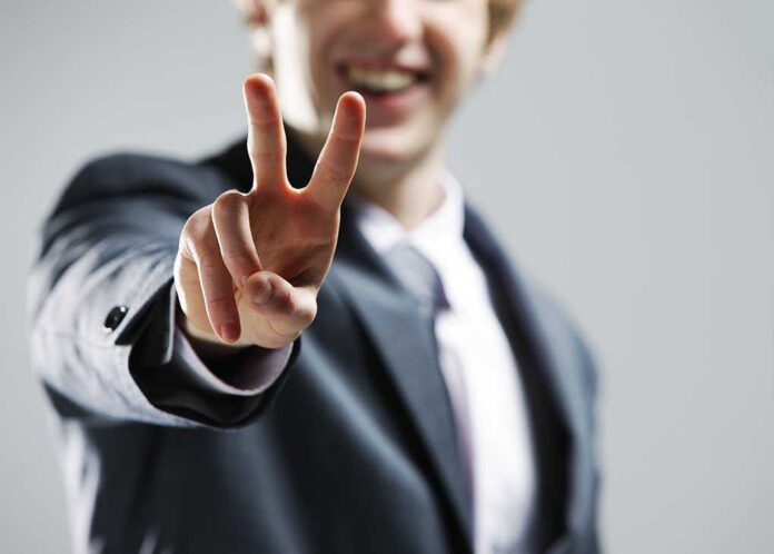 A man in a suit smiling and making a peace sign with his hand