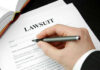 Hand holding pen, filling out lawsuit form.