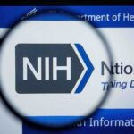 Viral Vaccine Claim — Real NIH Confession? NIH logo displayed on a digital screen, viewed through a magnifying glass
