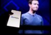 A hand holding a smartphone displaying the Meta logo with a blurred figure in the background
