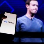 Digital ID Dragnet INCOMING — Meta THREATENED to Start A hand holding a smartphone displaying the Meta logo with a blurred figure in the background