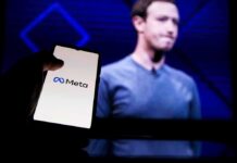 A hand holding a smartphone displaying the Meta logo with a blurred figure in the background