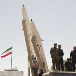 New Intelligence Warns: Missile Threat Isn’t Over Military personnel beside missiles and Iranian flag.