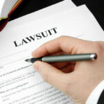 Hand holding pen, filling out lawsuit form.