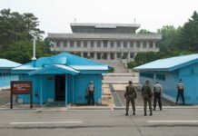 Military personnel standing near blue buildings at a border crossing