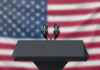 Anonymous Complaint: July 4 Military Flyover Probe Ends Podium with microphones, American flag background.