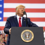 Mount Rushmore Fireworks, Culture War Erupts Man speaks at podium with U.S. flag background.