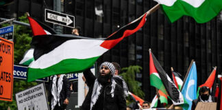 Protesters with flags and signs, one holding a megaphone.