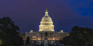 Illuminated capitol building at night with reflection in water.