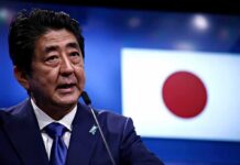 man speaking at podium with Japanese flag in background