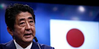man speaking at podium with Japanese flag in background