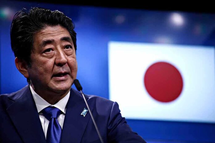 man speaking at podium with Japanese flag in background