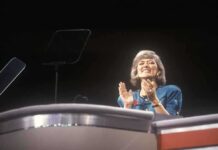 A female speaker on stage smiling and clapping during a presentation