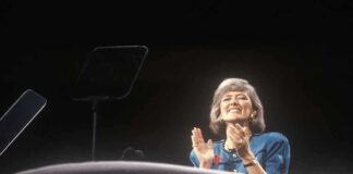 A female speaker on stage smiling and clapping during a presentation