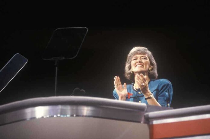 A female speaker on stage smiling and clapping during a presentation